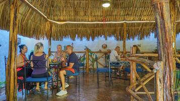 Un espacio de comedor al aire libre rústico, con techos de paja y mobiliario de madera.