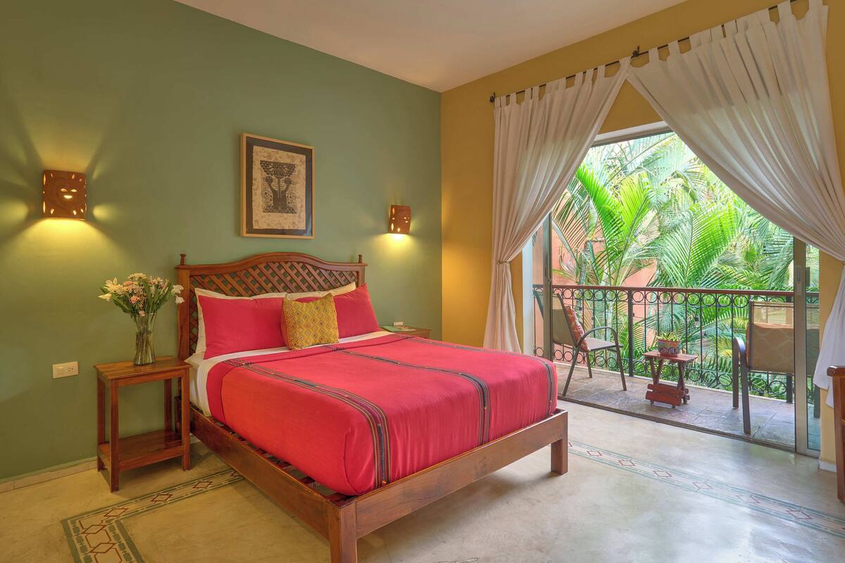 A bedroom with a wooden bed, a nightstand with a vase of flowers, and a view of a balcony with plants.