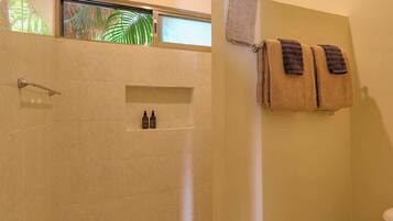 A bathroom with a shower, a toilet, and a window with a view of palm trees.