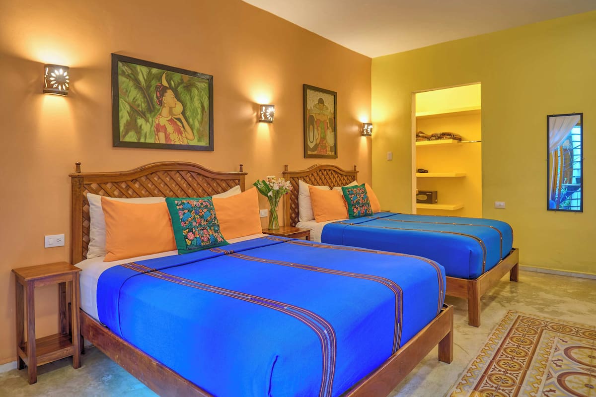 A hotel room with two wooden beds, orange and blue bedspreads, and decorative pillows.
