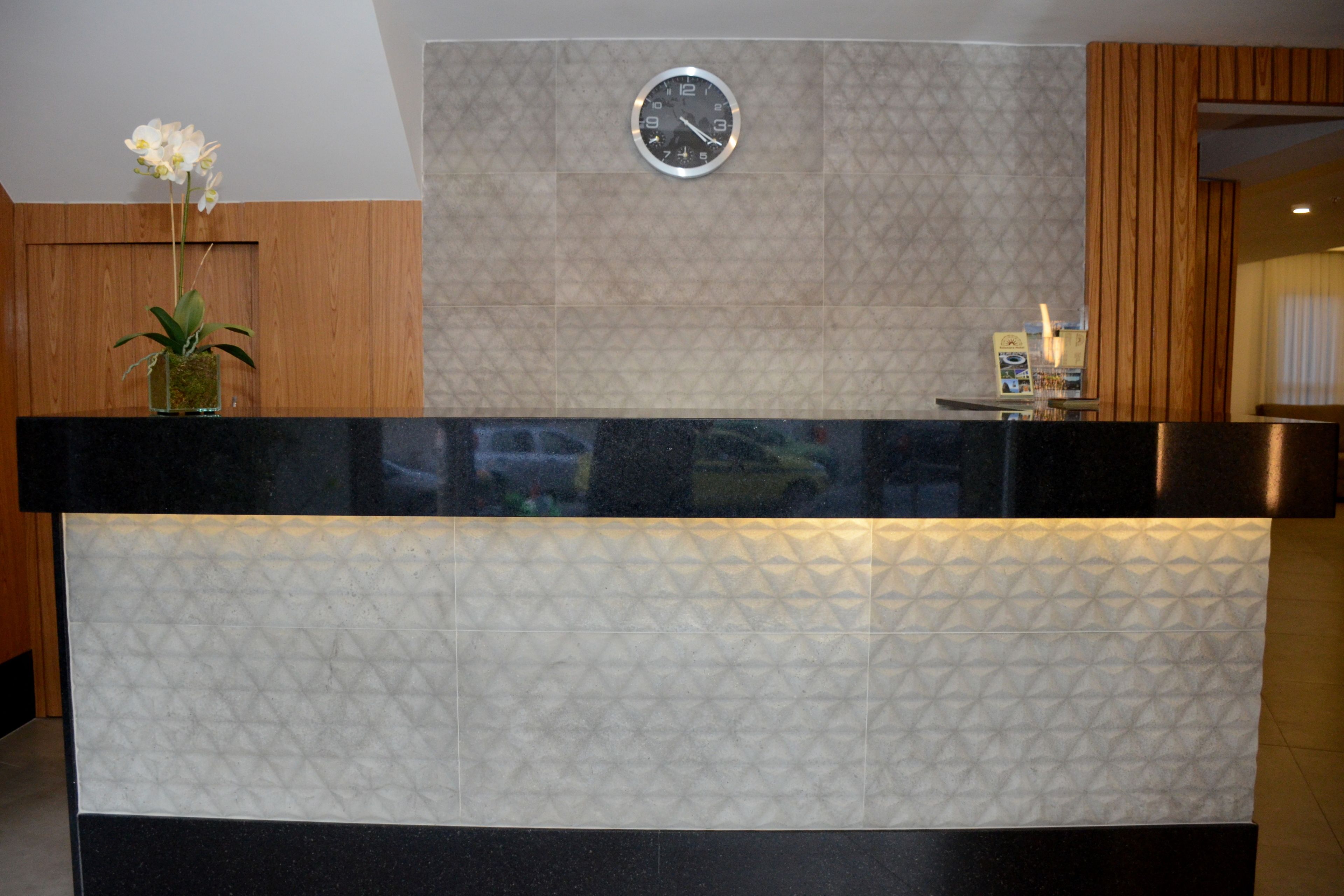 A reception desk with a clock, a vase with flowers, and a wooden panel wall.