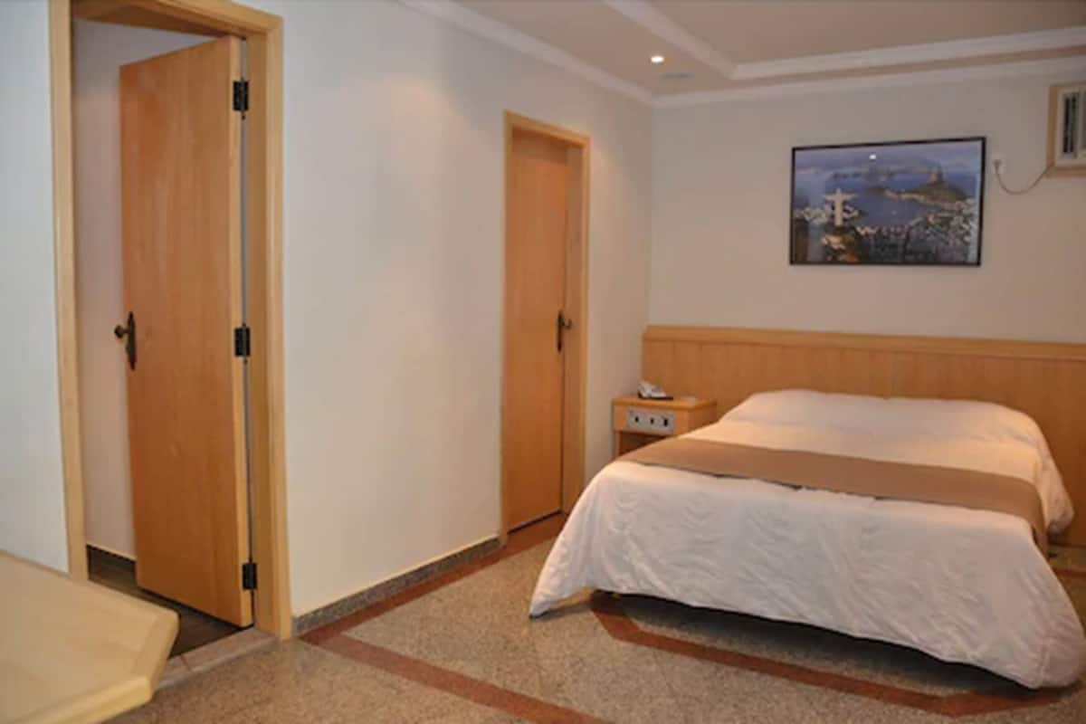 A hotel room with a bed, a nightstand, a wooden door, and a painting on the wall.