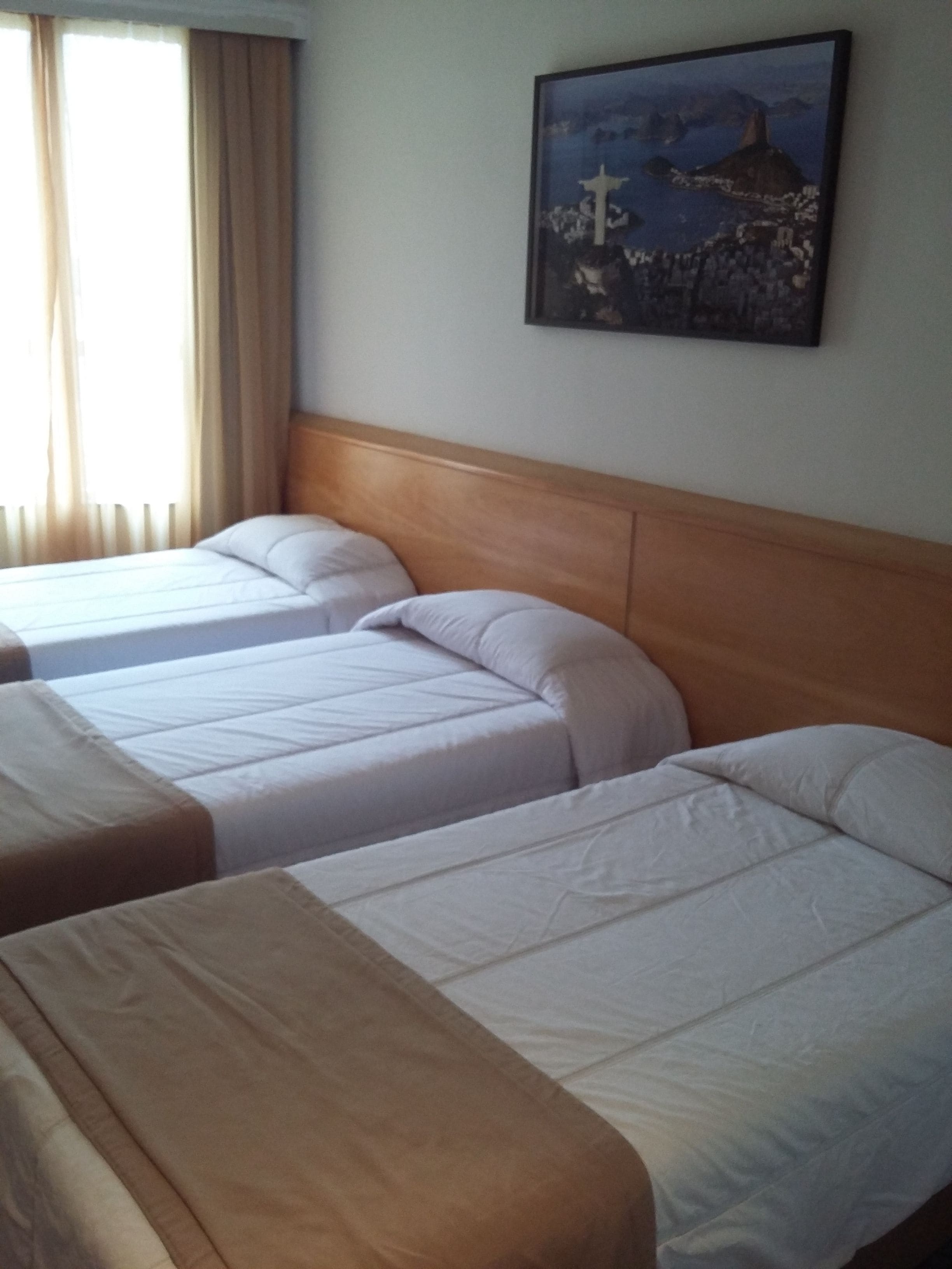 Habitación de hotel con dos camas individuales y una cama grande. En la pared, un cuadro que representa una escena costera.