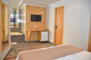 A hotel room with a bed, a small desk with a television, a mirror, and a door. - Saionara Hotel (Rio de Janeiro)