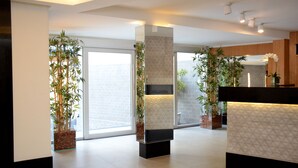 Un moderno vestíbulo de hotel con una recepción, ventanas amplias y plantas en macetas.