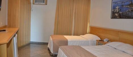 A hotel room with two beds, a desk, a chair, a window with curtains, and a painting on the wall.