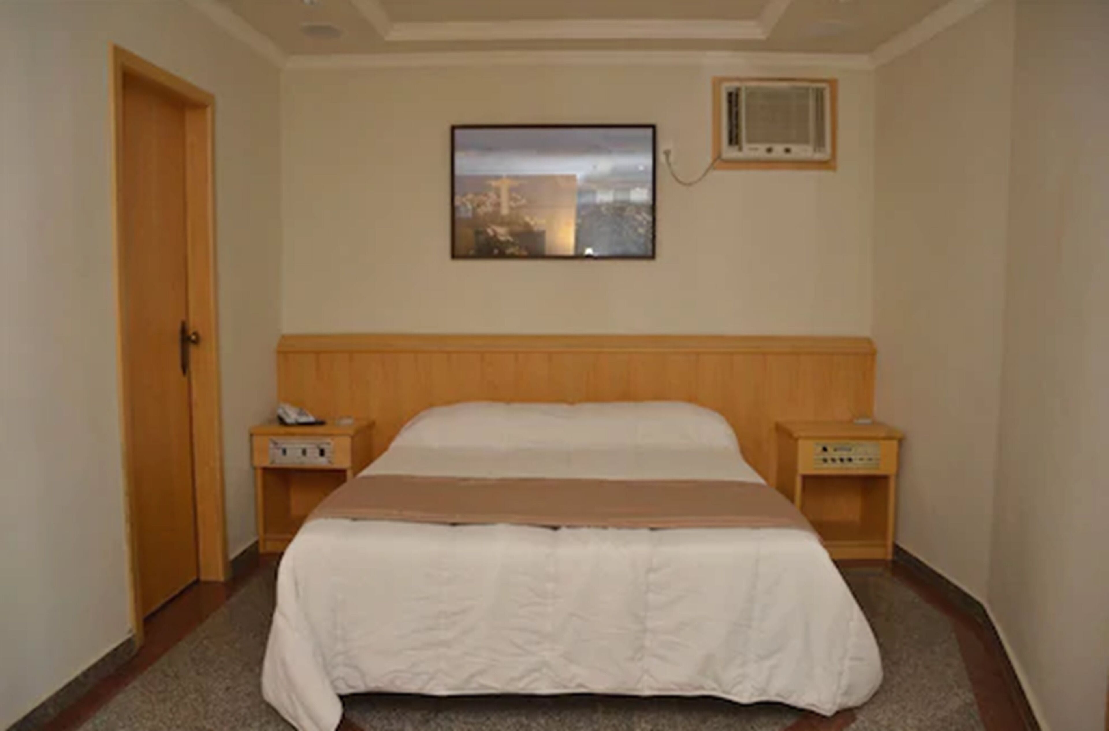 A hotel room with a bed, two bedside tables, a wall-mounted TV, and a door.