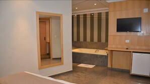 Habitación de hotel con cama, un escritorio pequeño, televisor y baño con bañera y ducha.