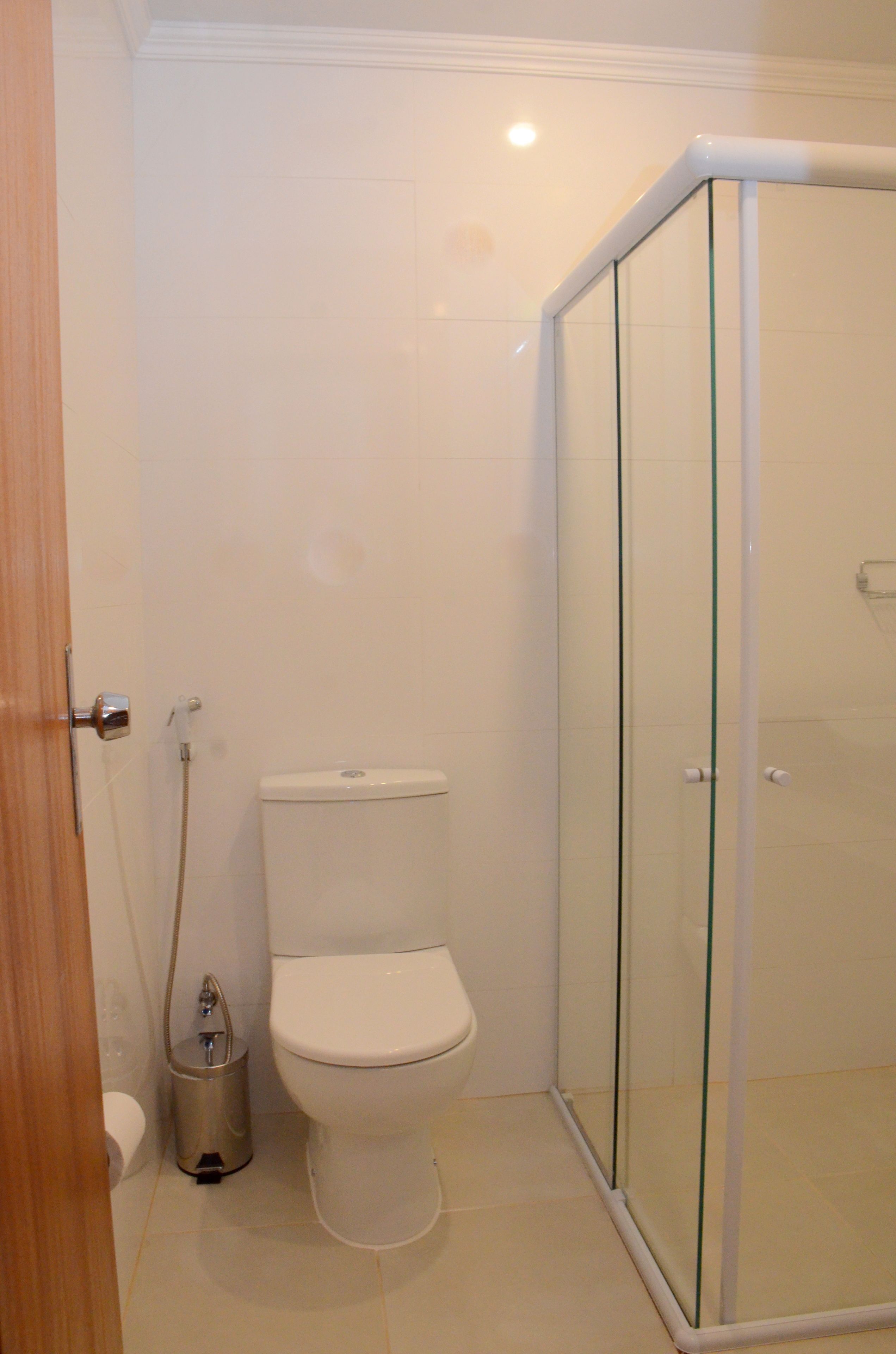 Een badkamer met een toilet, een glazen douchecabine en een prullenbak.