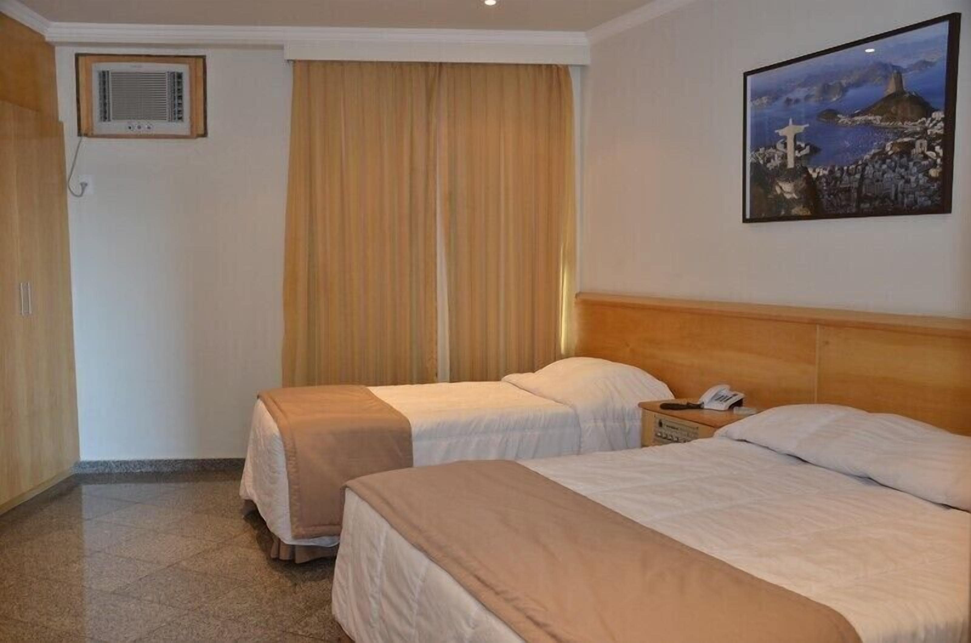 Habitación de hotel con dos camas, un cuadro en la pared y una ventana con cortinas.