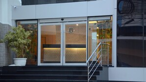 Entrada de un edificio con puerta de vidrio, un reloj y una escalera que sube.