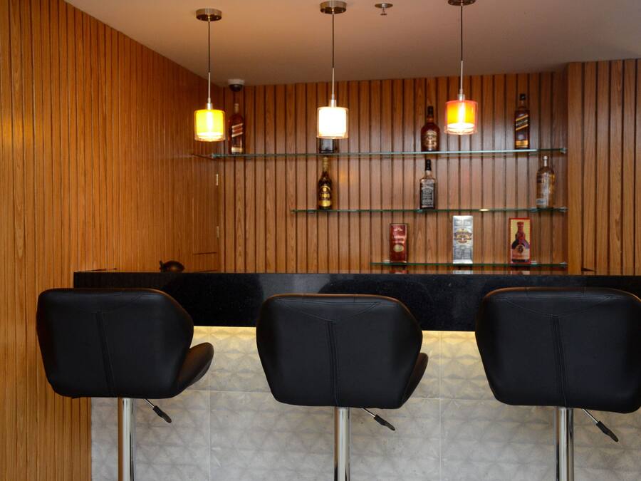Una zona de bar con paneles de madera, sillas de cuero negro y estantes con botellas.