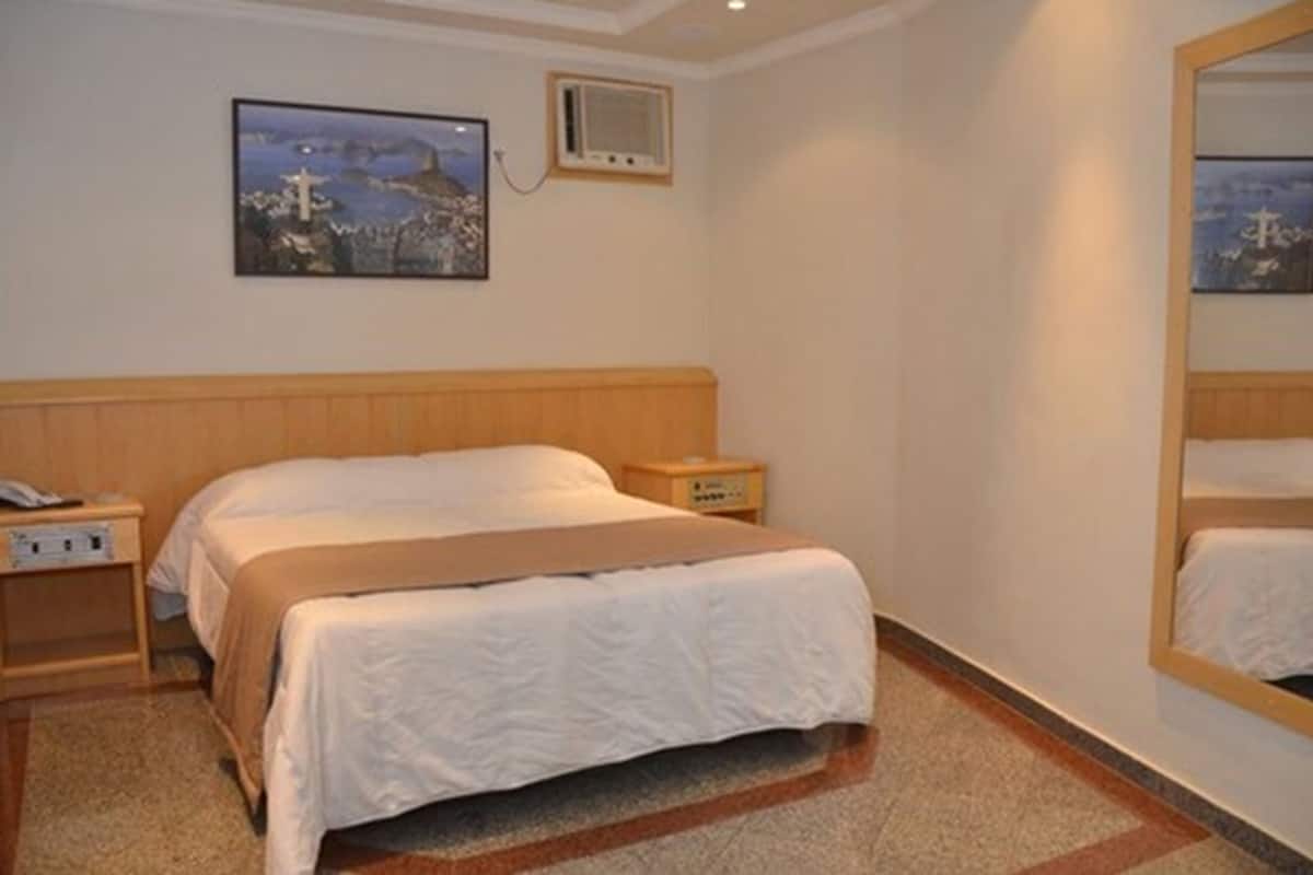 A bedroom with a bed, bedside table, nightstand, wall-mounted air conditioning unit, and a painting.