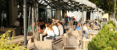 Een terras met tafels en stoelen, een overdekte doorgang en een bord met daarop een restaurant.