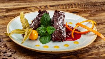Un plato con un postre de pastel de chocolate, hojas de menta, yema de huevo y ralladura de naranja sobre una mesa de madera.
