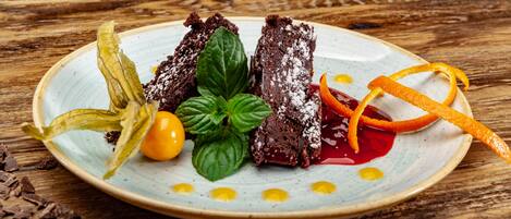 Un plato con un postre de pastel de chocolate, hojas de menta, yema de huevo y ralladura de naranja sobre una mesa de madera.