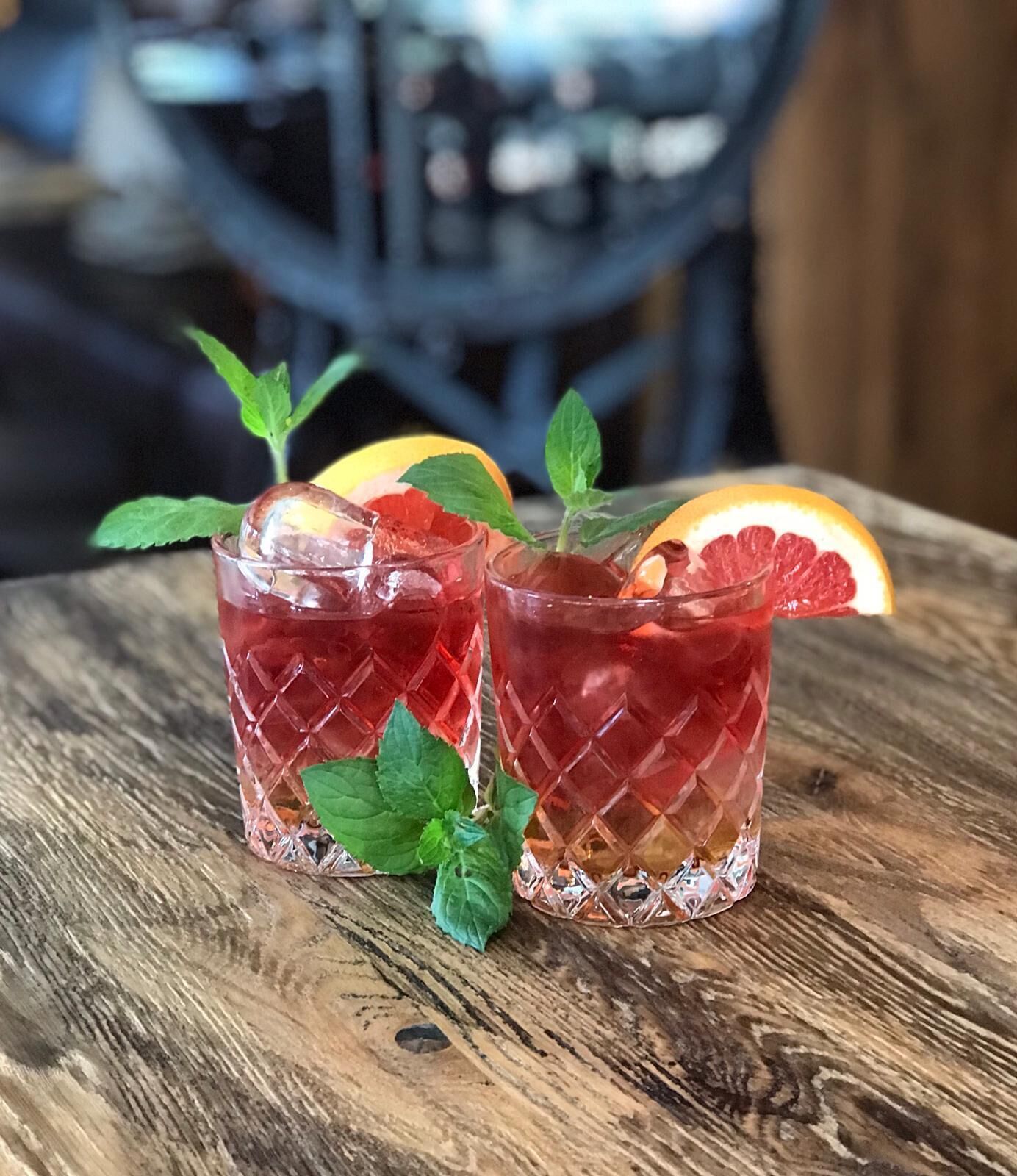 Twee glazen rode drank met muntblaadjes en citruspartjes op een houten tafel.