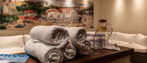 Una mesa ordenada con toallas enrolladas, un jarro de vidrio y una revista en una habitación de hotel.