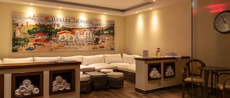 A modern hotel lobby with a large mural, a seating area with a sofa and chairs, and a small table with a vase.