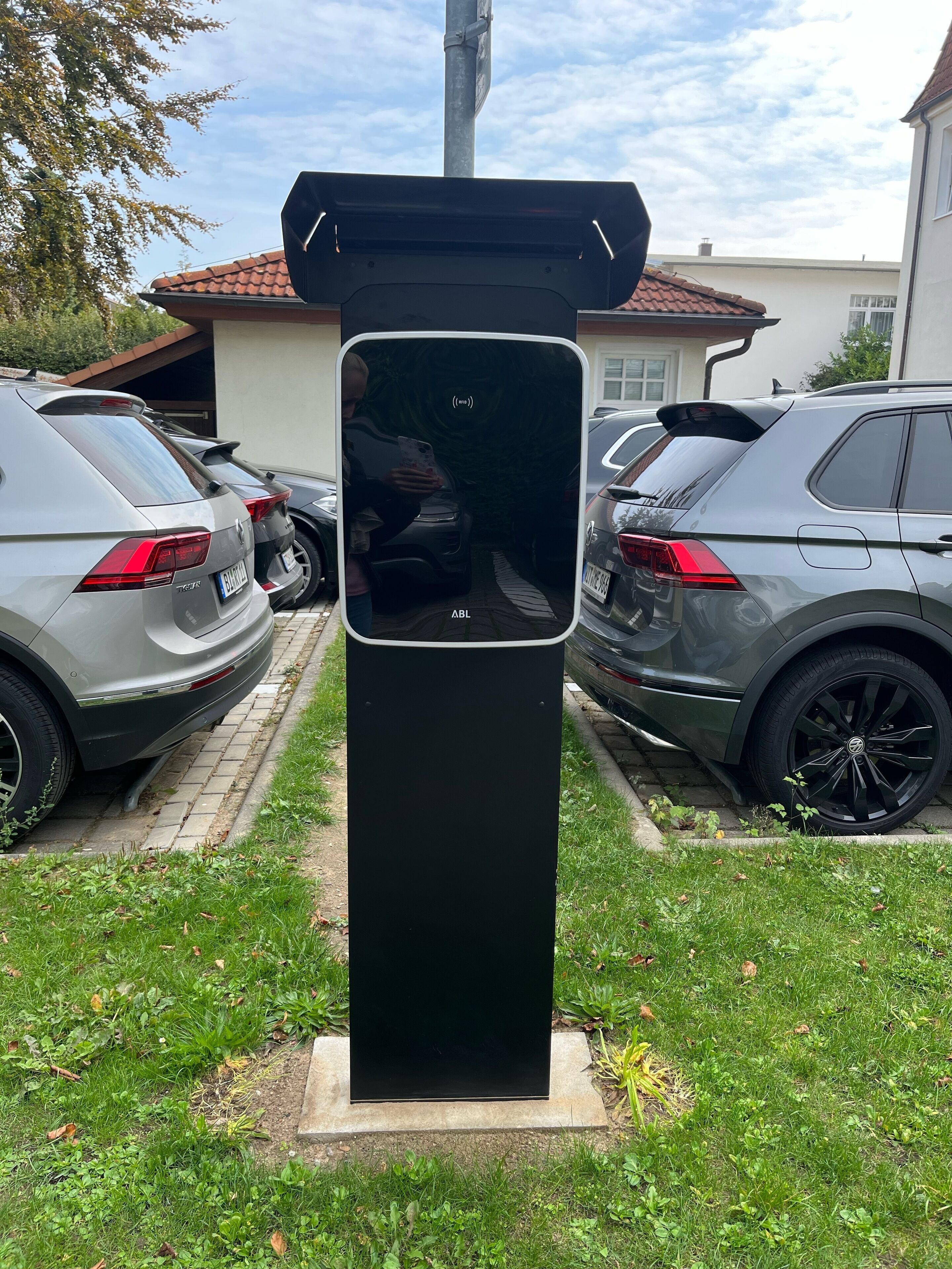 A black electric vehicle charging station in a residential area with cars parked nearby.