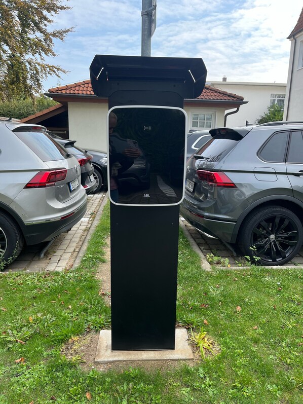 Una estación de carga para vehículos eléctricos negros en un barrio residencial, con automóviles estacionados cerca.