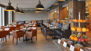 Un restaurant avec des tables rondes et des chaises orange, un mur en briques et un présentoir de fruits.