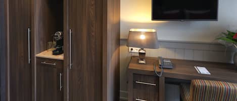 A hotel room with a wooden wardrobe, a desk with a lamp, a telephone, and a TV mounted on the wall.