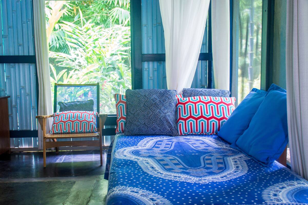 Una habitación con cama, una silla y vistas a la vegetación a través de amplios ventanales.
