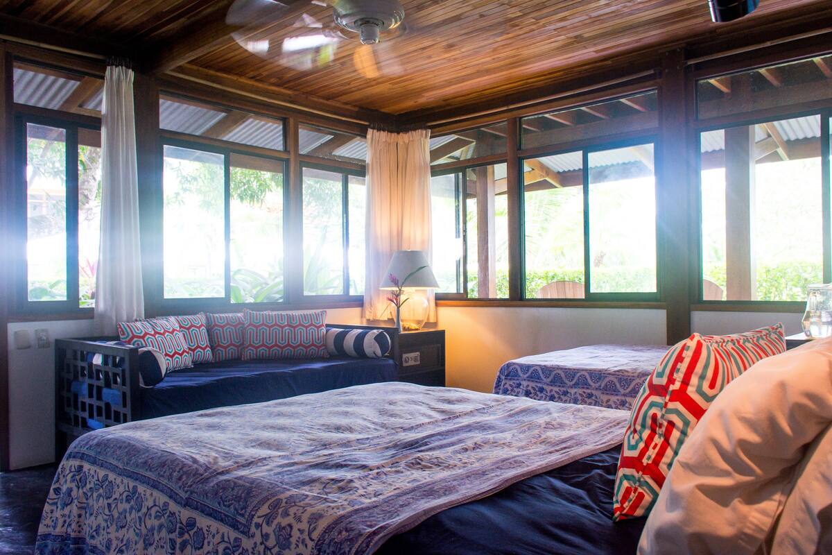 Una habitación con dos camas, techo de madera y ventanas amplias.