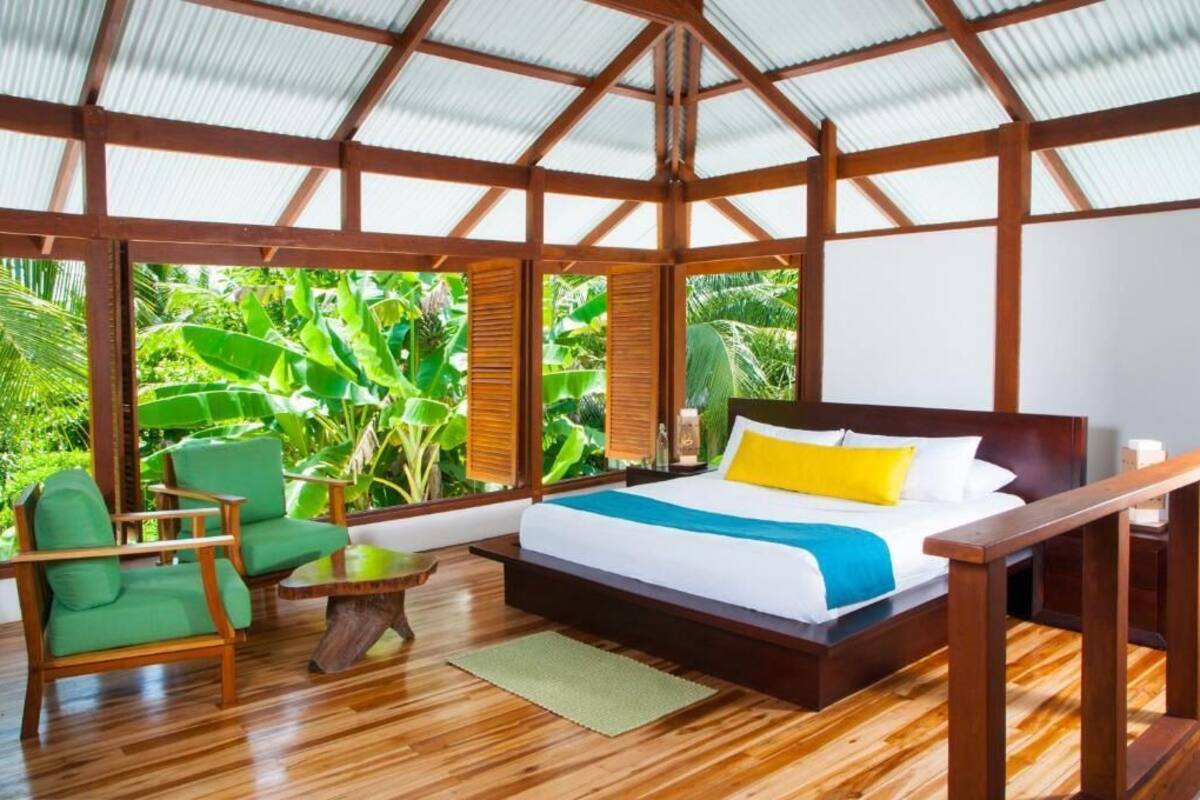 Una habitación amplia con una cama grande, muebles de madera y vistas a vegetación exuberante.