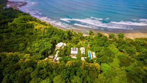 An aerial view of a coastal area with a beach, lush greenery, and several buildings with solar panels. - Blue Osa Beach Resort and Spa (Puerto Jiménez)