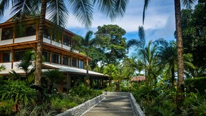 A two-story house with a covered porch, surrounded by lush tropical vegetation and a stone pathway leading to the entrance. - Blue Osa Beach Resort and Spa (Puerto Jiménez)