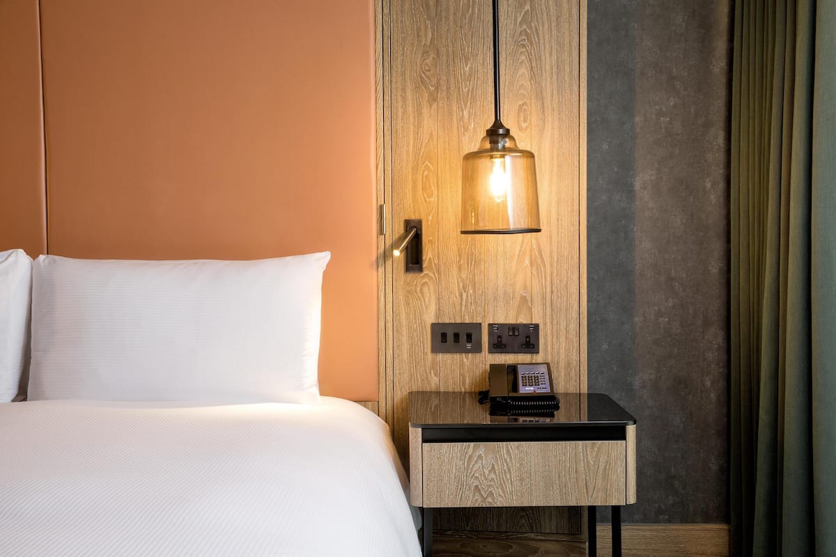Habitación de hotel con cama, mesita de noche, teléfono y lámpara fijada a la pared.