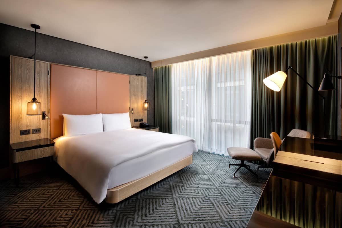 Una habitación de hotel con una cama grande, un escritorio, una silla, un armario y una lámpara.