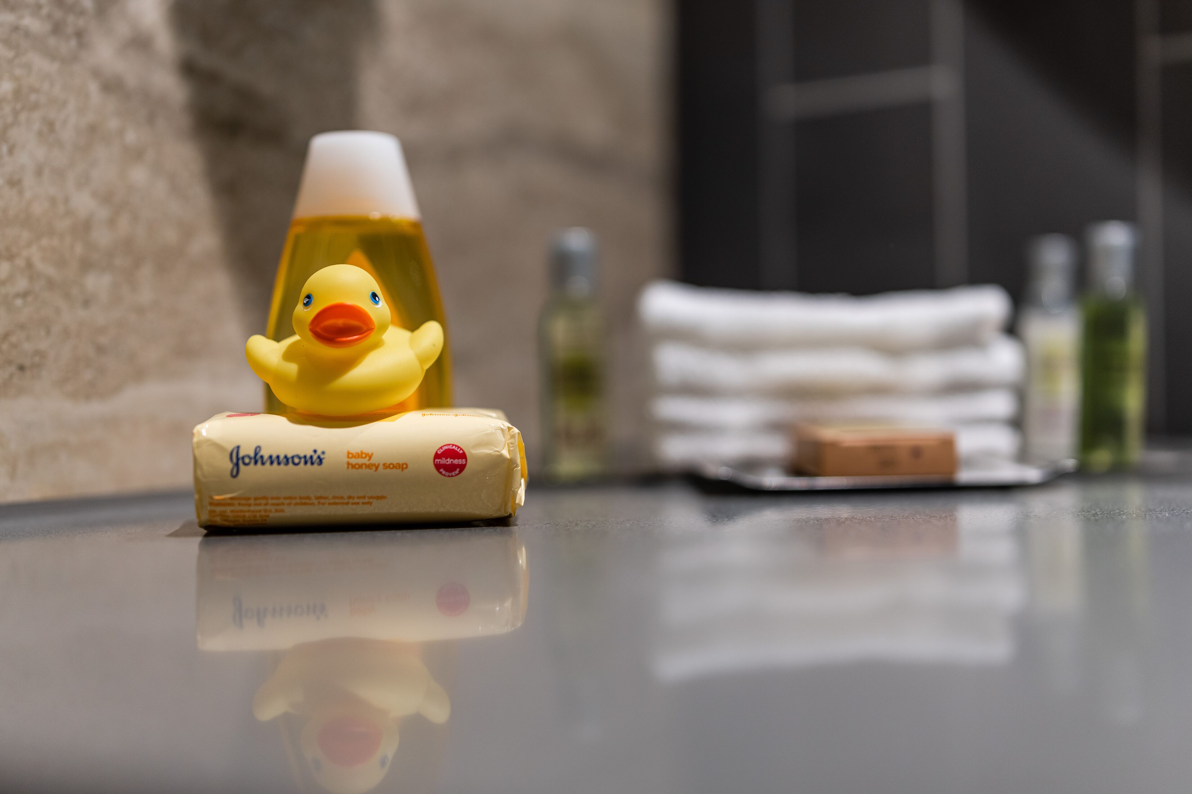 A bathroom counter with a rubber duck, a baby soap bar, a towel, and some toiletries.