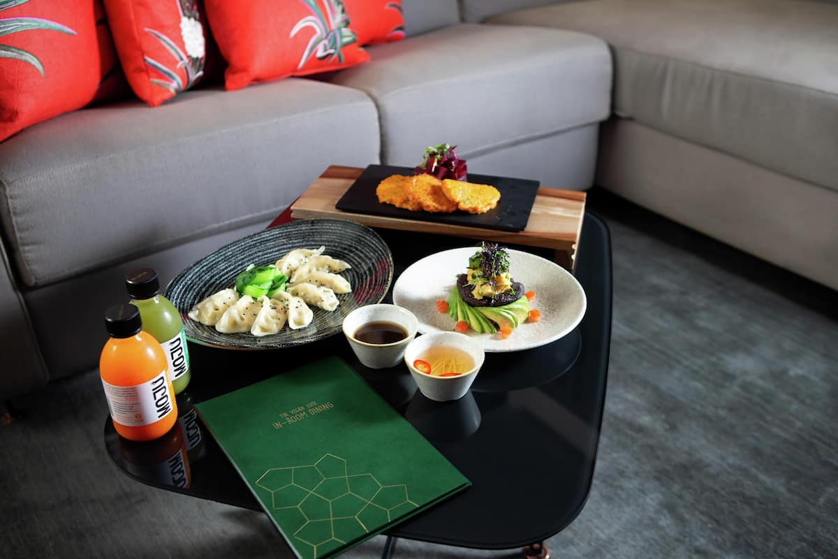 Una mesa de comedor con un menú, una botella de jugo de naranja, un bol de dumplings, un plato de verduras y un recipiente pequeño con salsa.