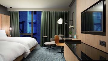 A hotel room with a large bed, a desk with a chair, a TV, and a view of a building through the window.