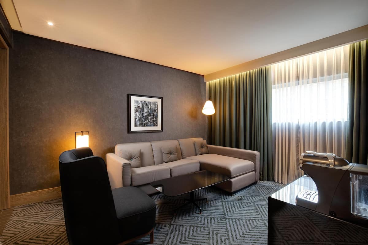 Una habitación de hotel moderna con sofá, sillón y una mesa de centro de vidrio.