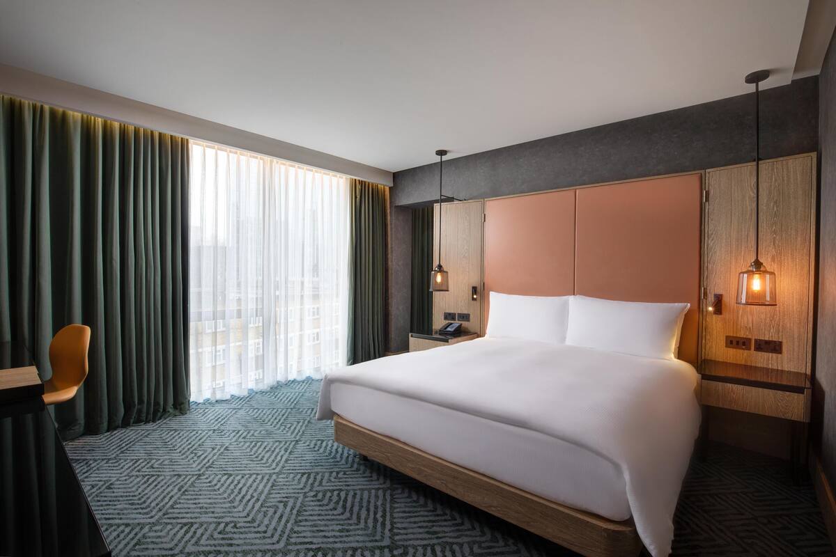 Una habitación de hotel con una cama grande, un escritorio, una silla, una mesita de noche y un armario.
