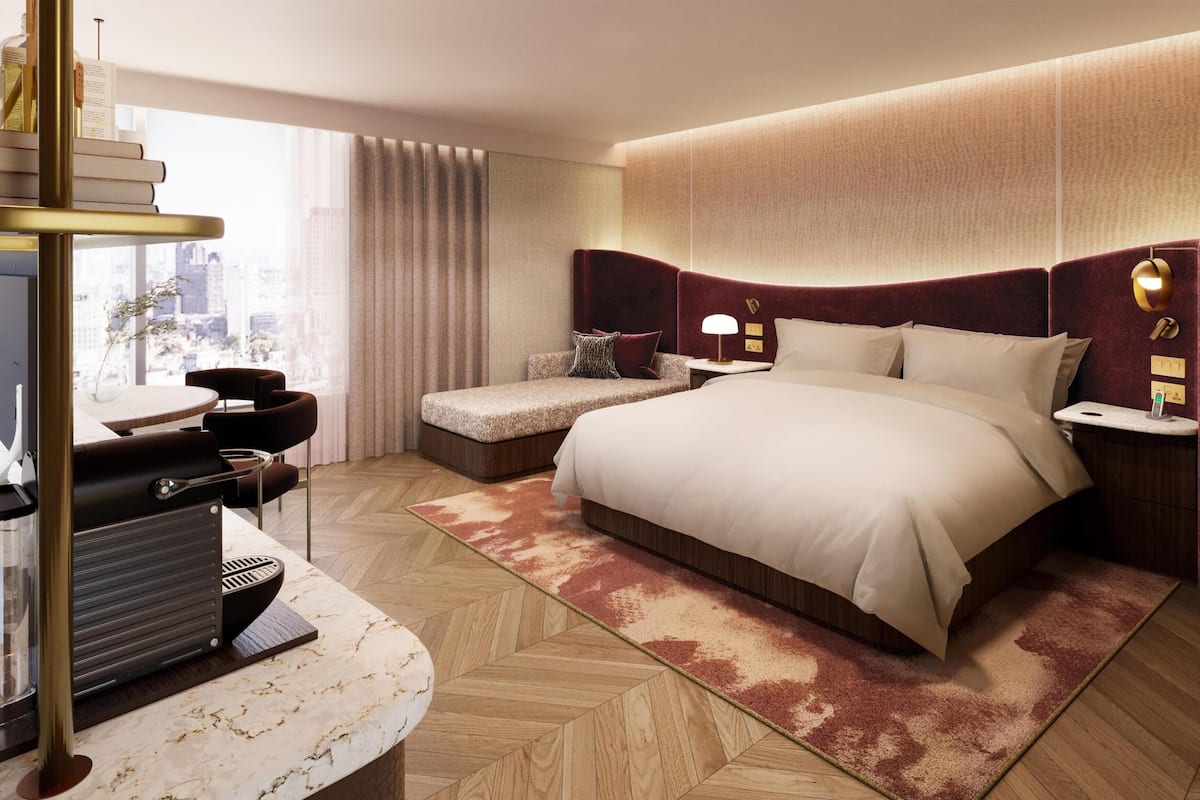 Una habitación de hotel moderna con una cama grande, un escritorio con una computadora portátil, una silla y vistas de la ciudad a través de grandes ventanales.