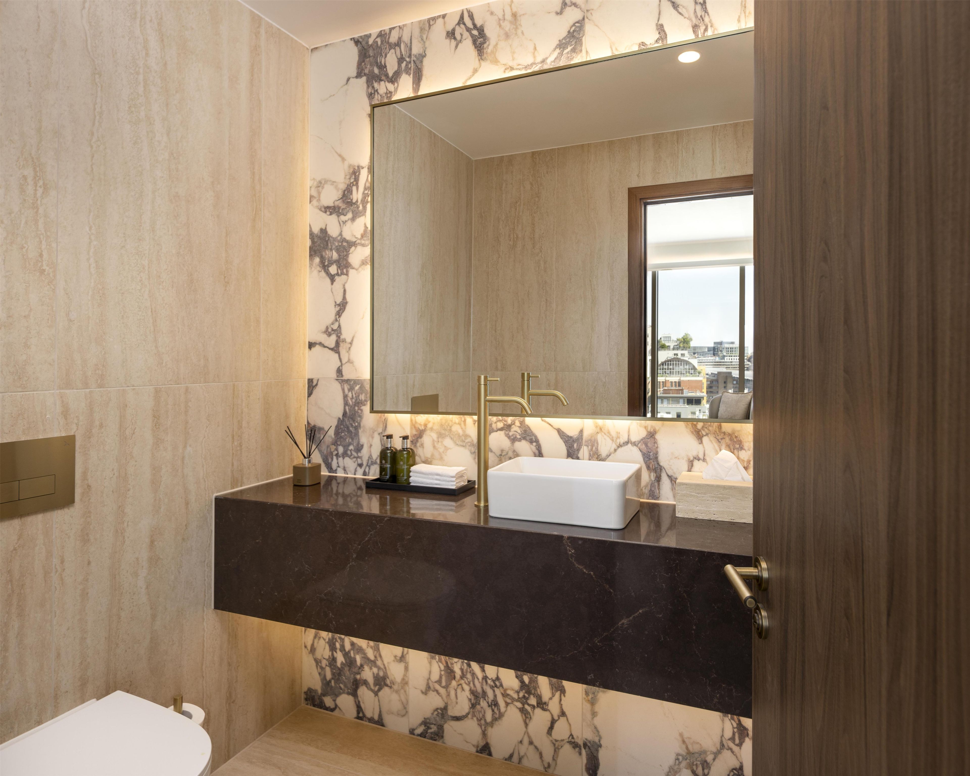 Ein modernes Badezimmer mit einem Marmor-Waschtisch, einem großen Spiegel und Blick auf die Stadt durch das Fenster.
