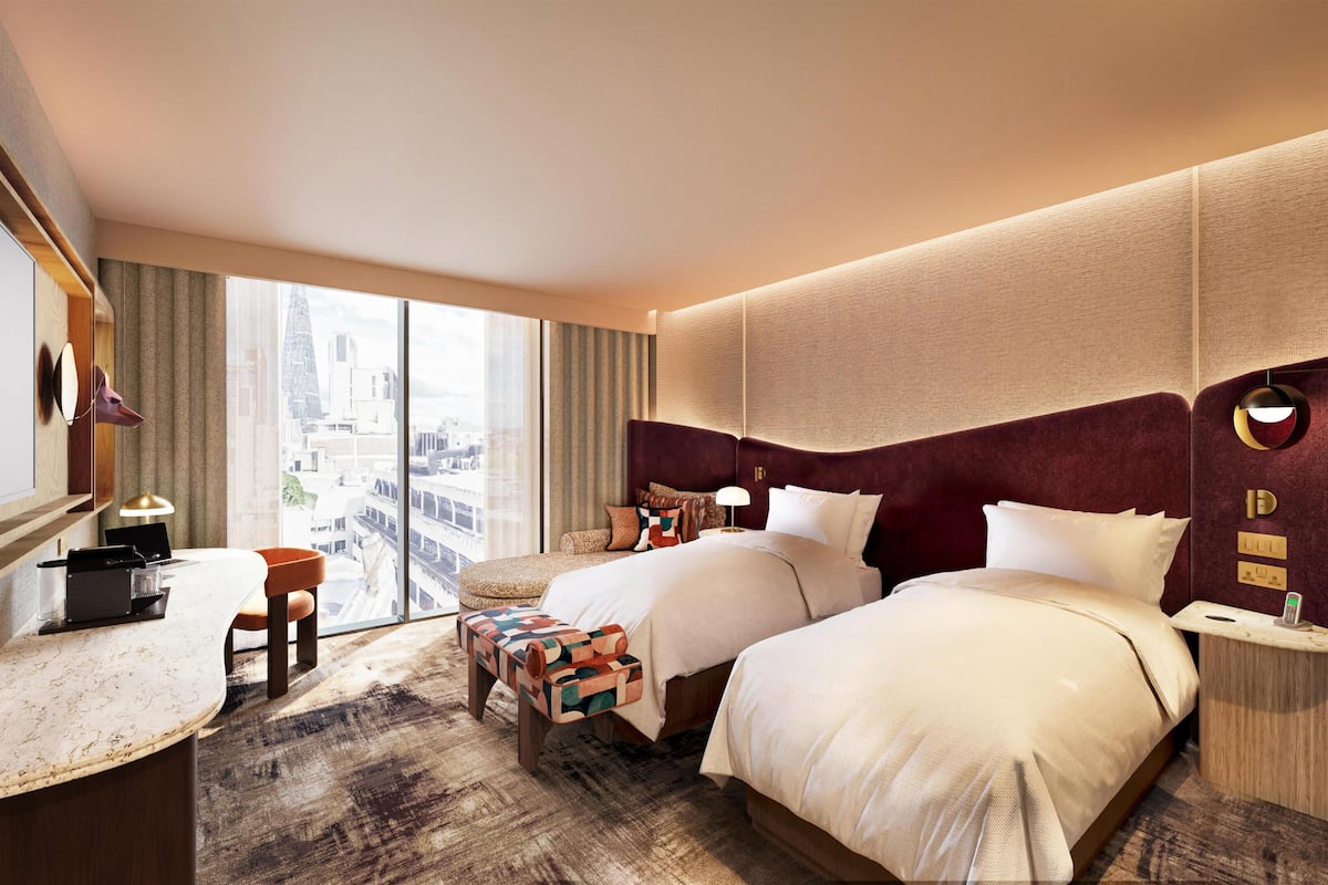 Habitación de hotel con una cama grande, un escritorio con una computadora portátil, una silla y vistas a la ciudad.