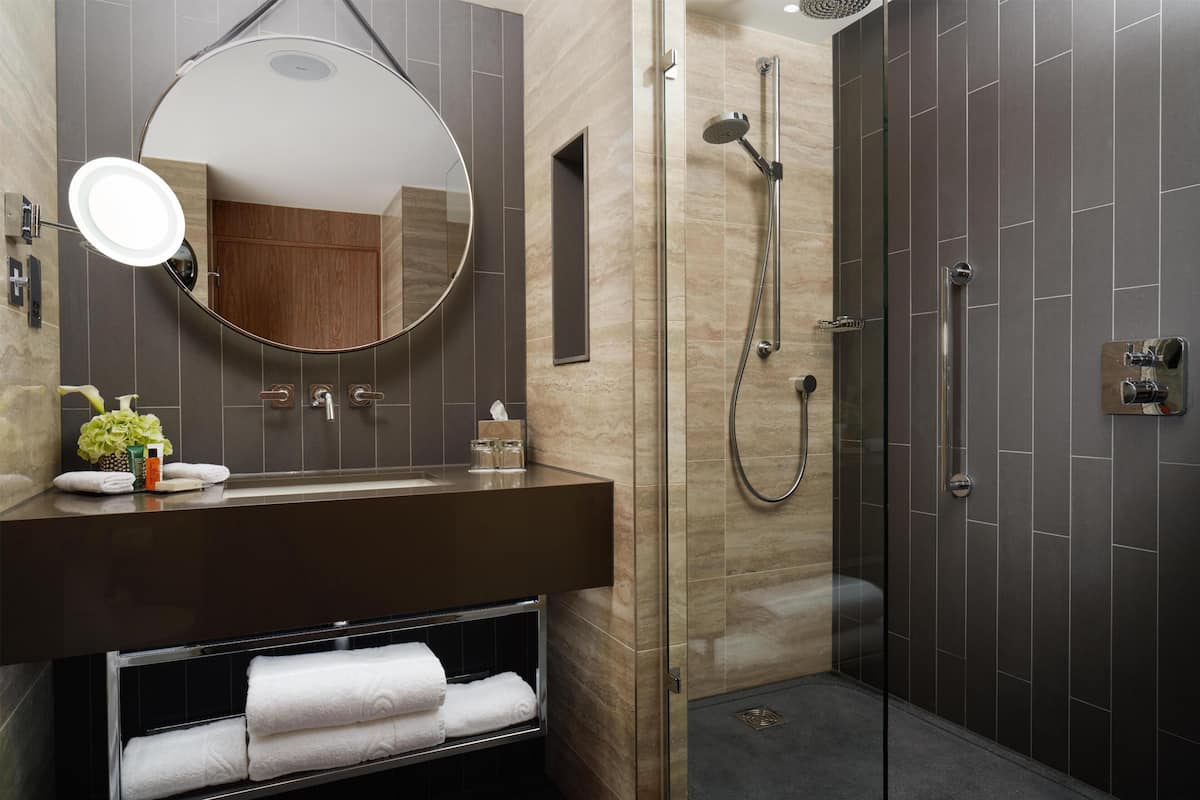 Un baño moderno con un espejo redondo, una ducha con puerta de vidrio y un mueble de tocador color marrón oscuro.
