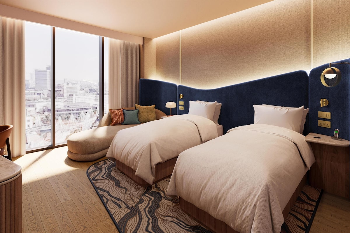 Habitación de hotel con dos camas, un escritorio, una silla, vistas a la ciudad y una alfombra estampada.