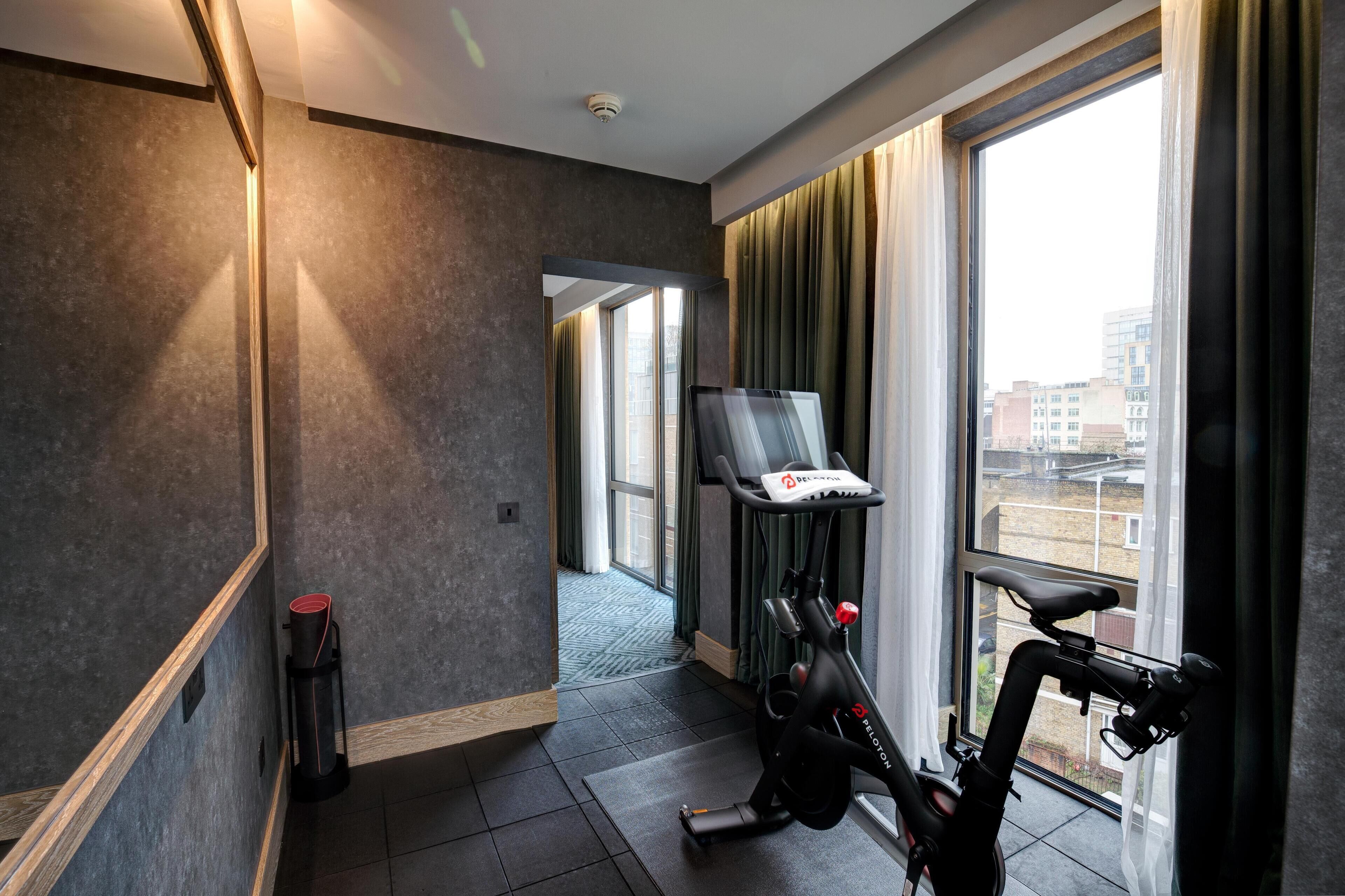 Une chambre d’hôtel moderne dotée d’une grande fenêtre, d’un tapis de course, d’un miroir et d’une porte donnant sur une autre pièce.