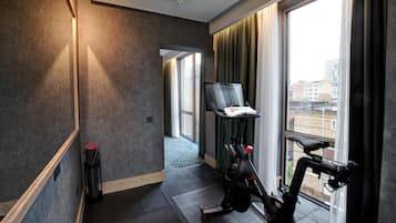 A modern hotel room with a large window, a treadmill, a mirror, and a door leading to another room.