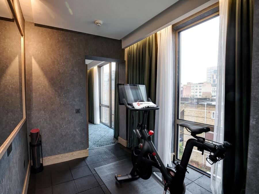 Une chambre d’hôtel moderne dotée d’une grande fenêtre, d’un tapis de course, d’un miroir et d’une porte donnant sur une autre pièce.