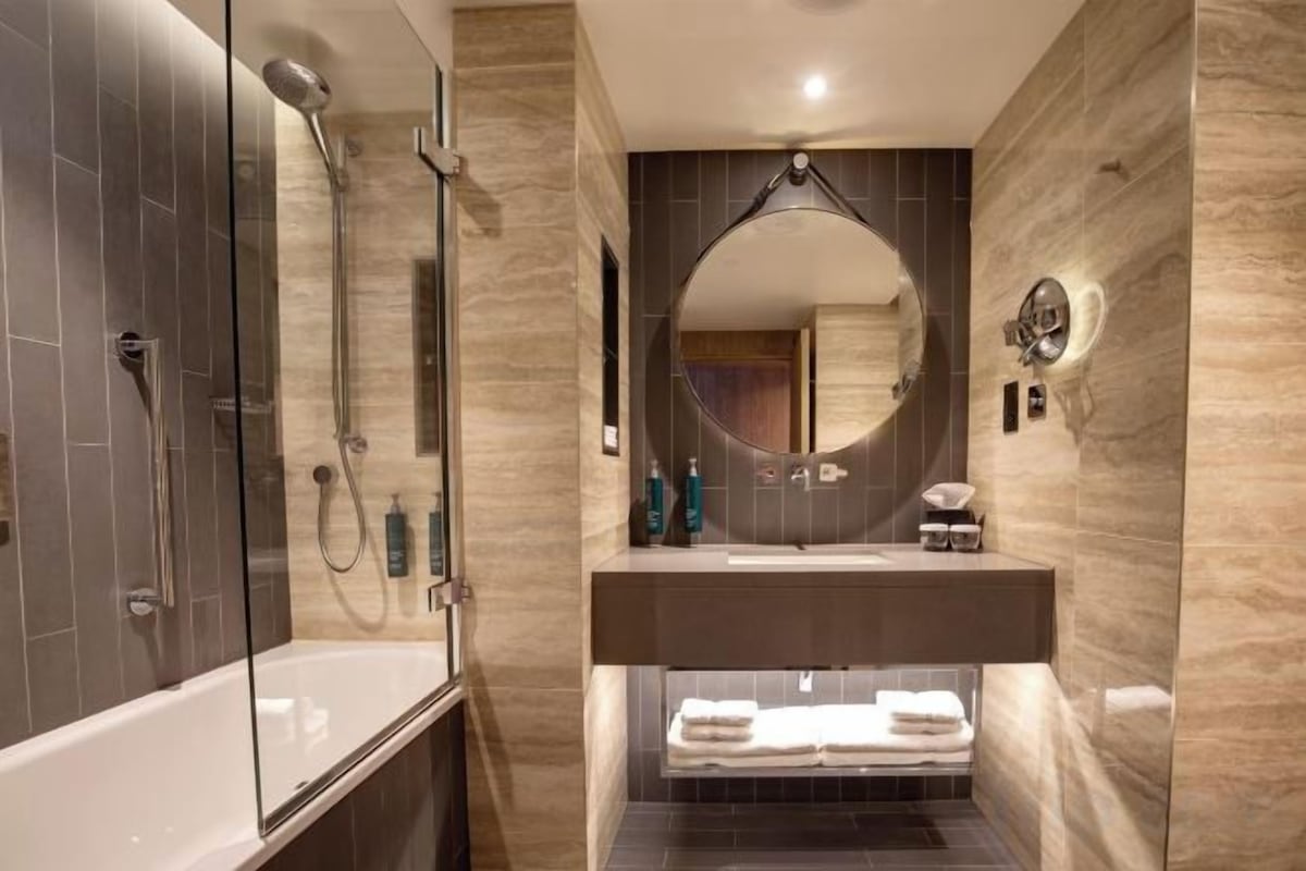 A modern bathroom with a glass-enclosed shower, a freestanding bathtub, a vanity with a mirror, and a towel rack.