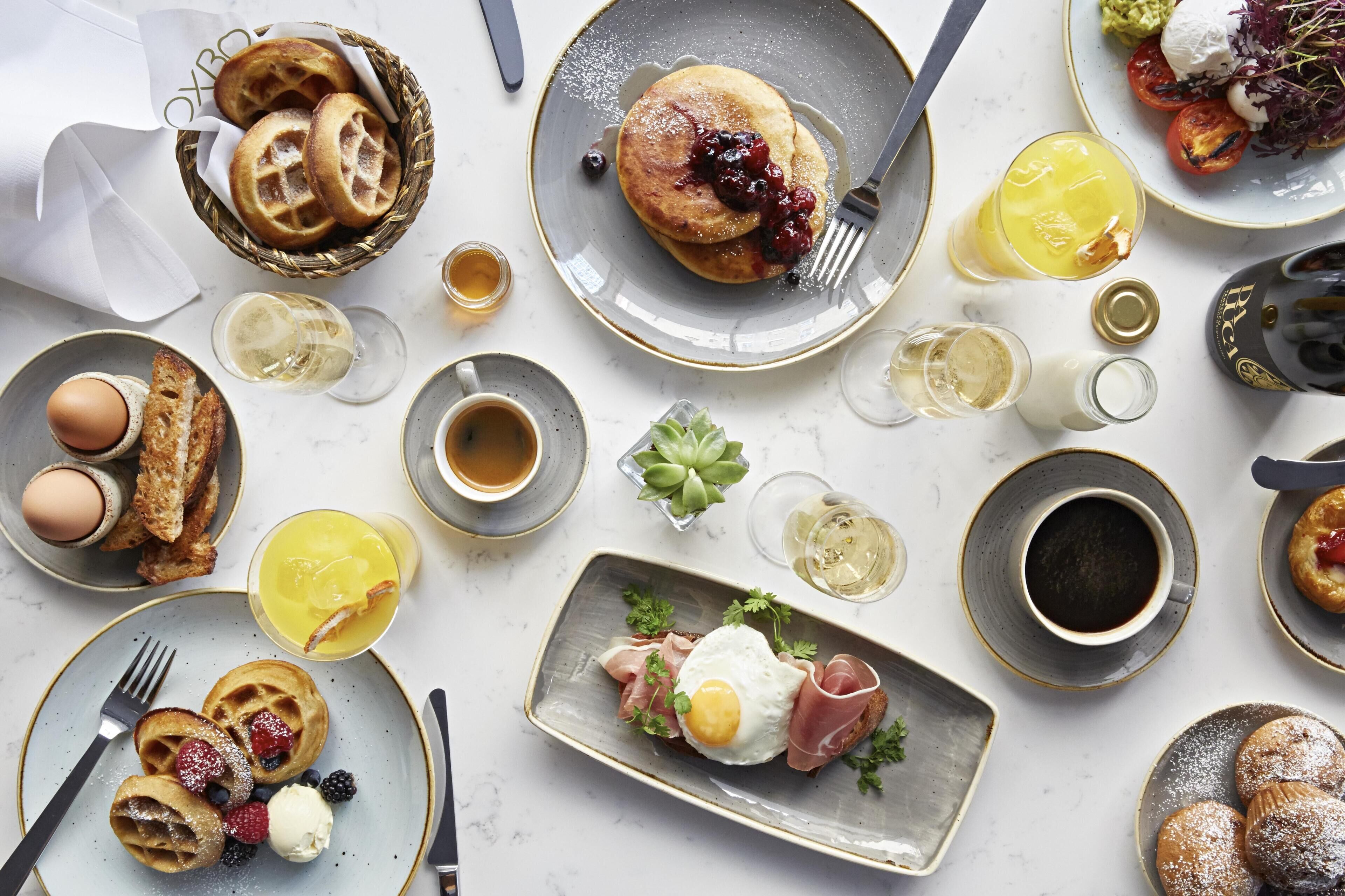 Una mesa con waffles, huevos y diferentes frutas.