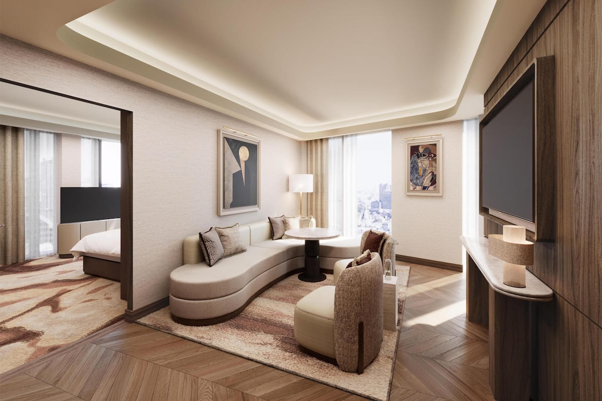 Habitación de hotel moderna con sofá curvo, televisor de pantalla plana, mesa de comedor y obras de arte en las paredes.